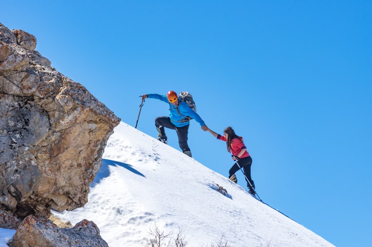 one climber helping another climber up a snowy mountain