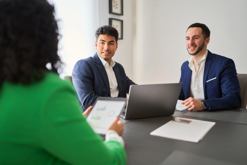 Three professionals are sitting at a table, one of them holding a tablet.